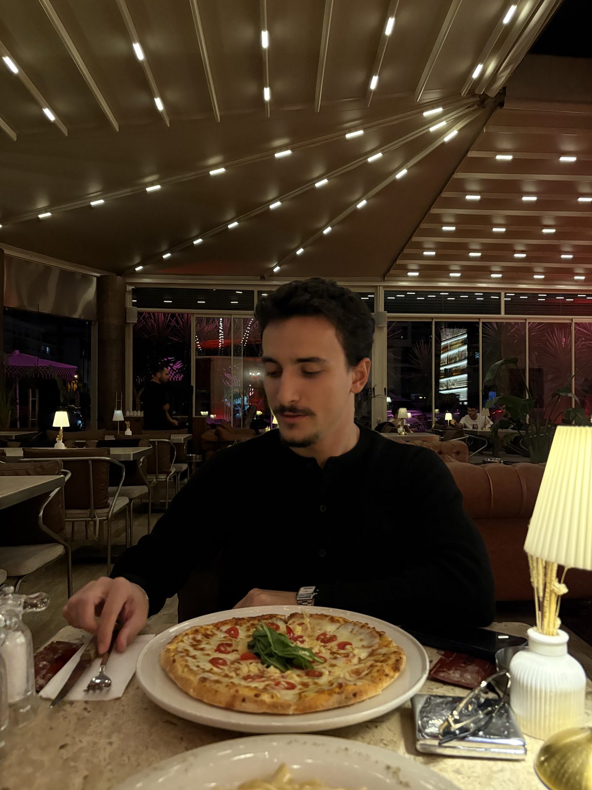 Eray Pişkin at a restaurant table at night, a pizza in front of him.