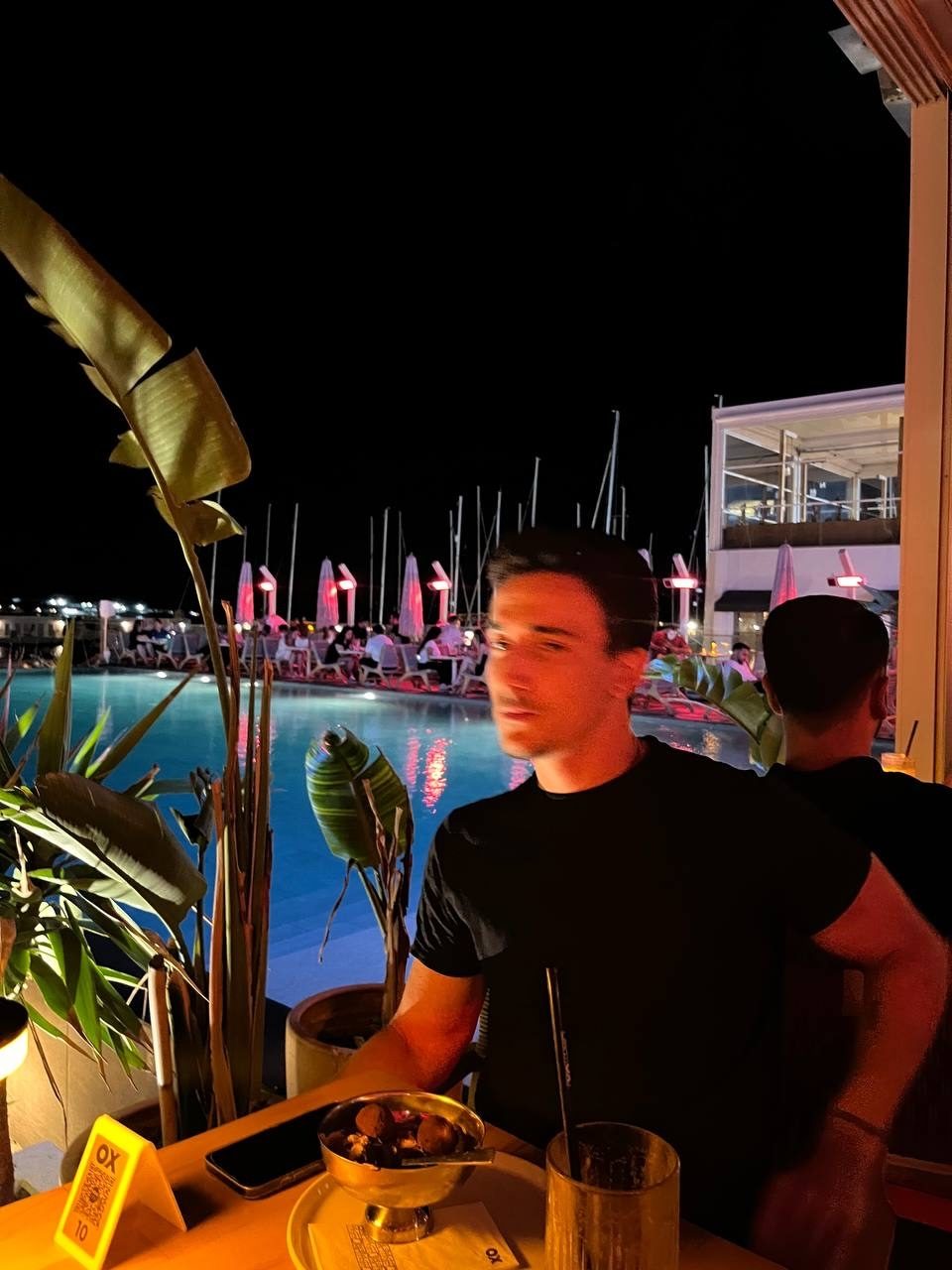 Eray Pişkin at a poolside bar at night, boats and lights behind him.