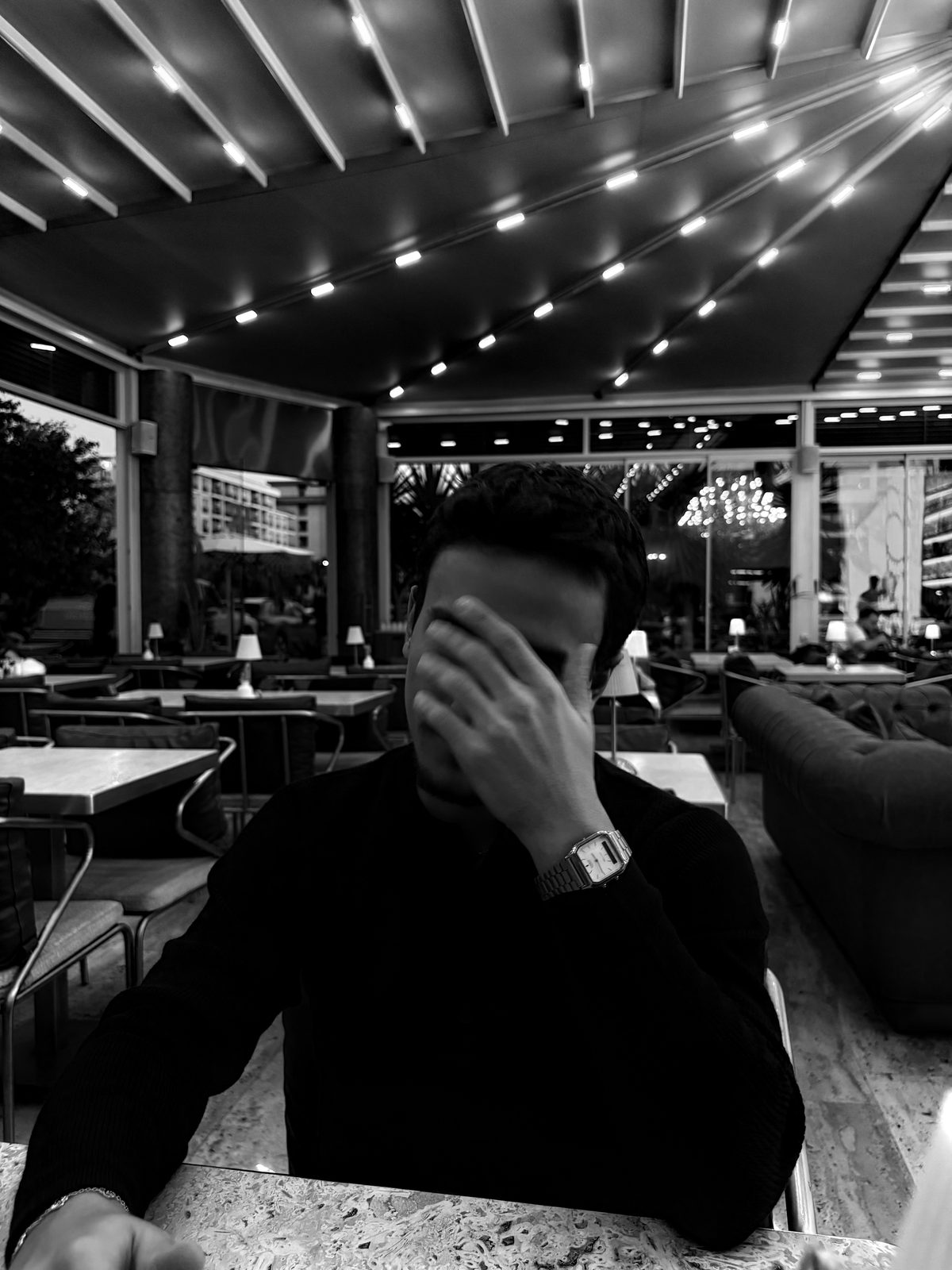 Eray Pişkin seated at a table with a hand across his face, in black and white.